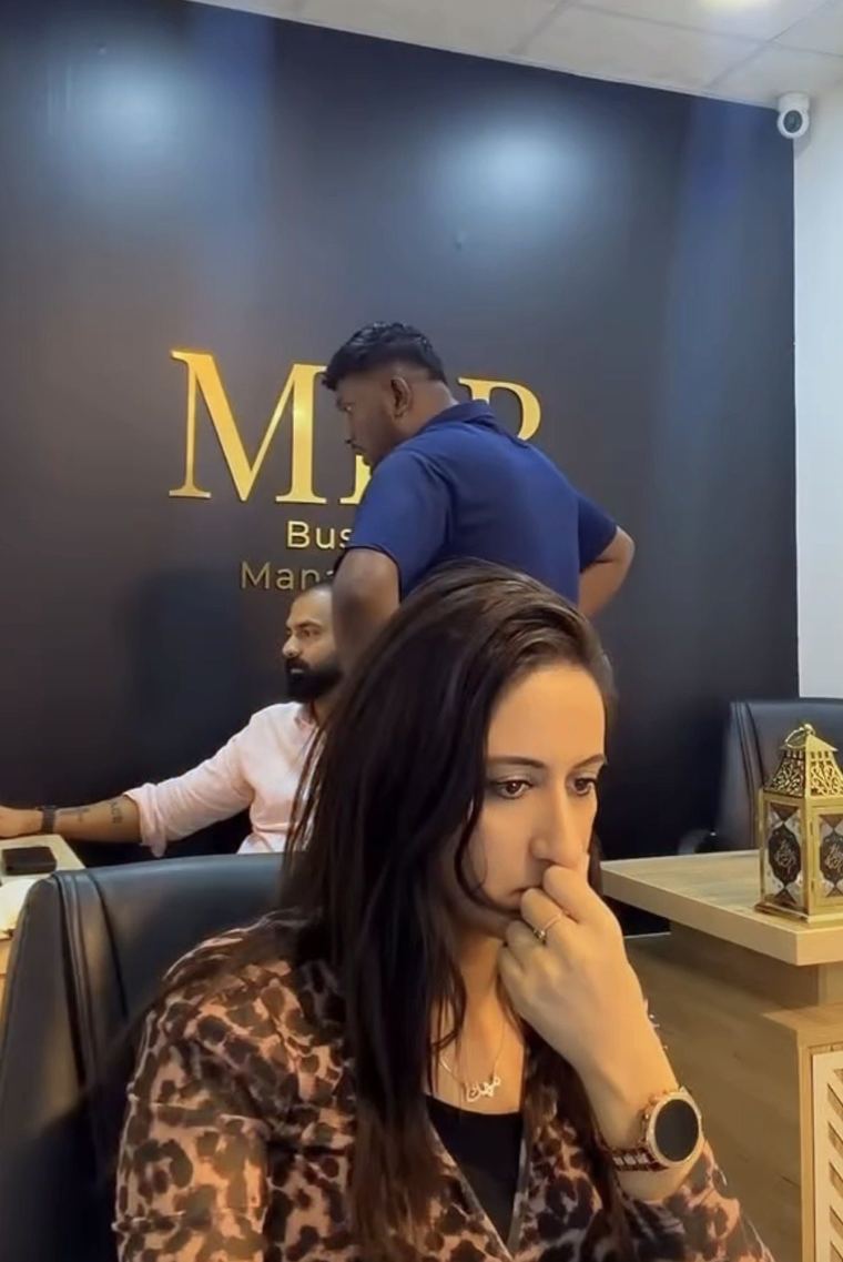 مهك بت تراجع ملف أحد العملاء في مكتب الاستقبال بينما يعمل الفريق خلفها